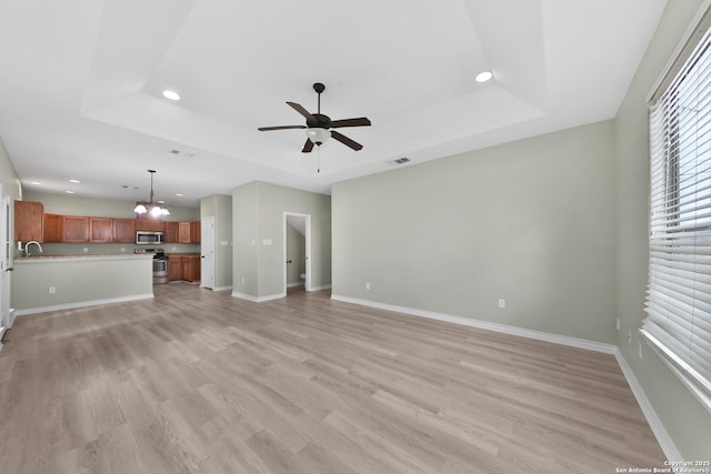 unfurnished living room featuring ceiling fan with notable chandelier, a raised ceiling, and light hardwood / wood-style floors