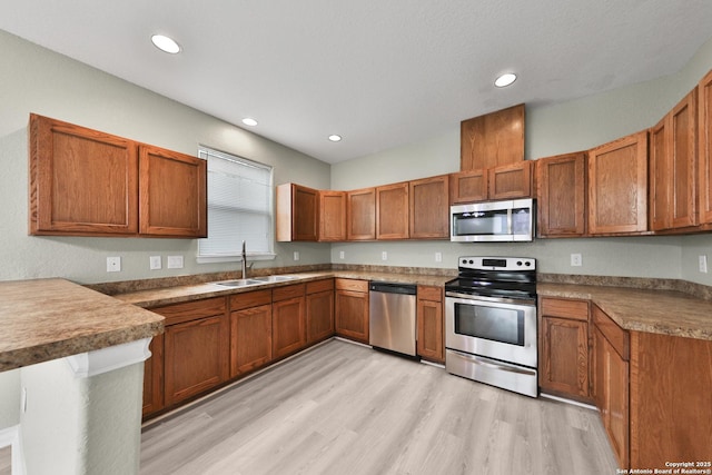 kitchen featuring sink, appliances with stainless steel finishes, a kitchen bar, kitchen peninsula, and light wood-type flooring