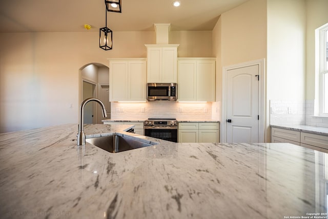 kitchen featuring decorative light fixtures, white cabinetry, sink, light stone counters, and stainless steel appliances