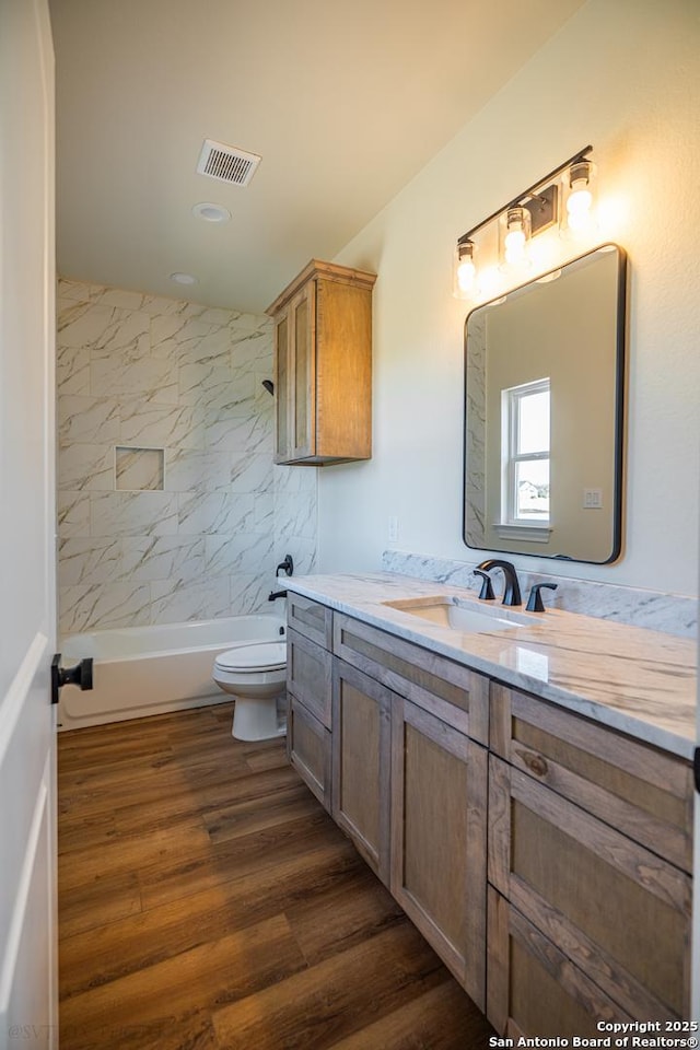 full bathroom featuring vanity, hardwood / wood-style floors, tiled shower / bath combo, and toilet