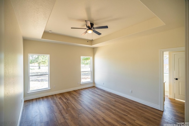 empty room with a raised ceiling, ceiling fan, and dark hardwood / wood-style flooring