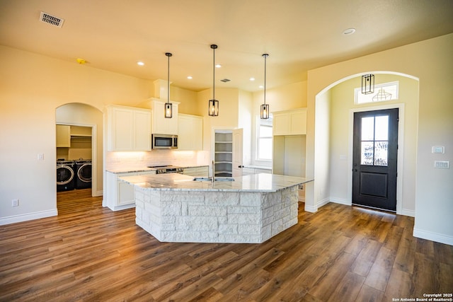 kitchen with washer and dryer, stainless steel appliances, a center island with sink, and white cabinets