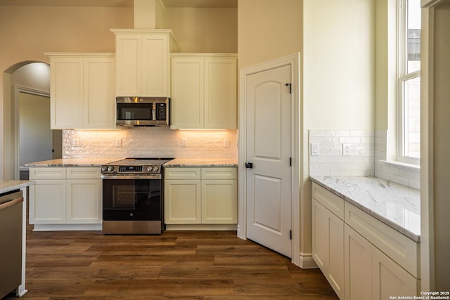 kitchen with dark wood-type flooring, backsplash, stainless steel appliances, light stone countertops, and white cabinets