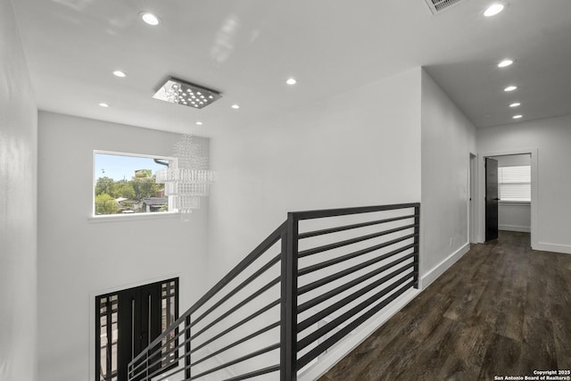 corridor with dark wood-type flooring, a wealth of natural light, and an inviting chandelier