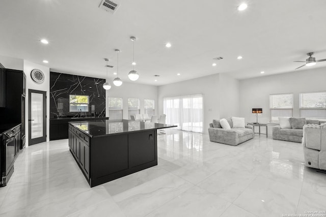 kitchen featuring ceiling fan, a center island, dark stone counters, and decorative light fixtures