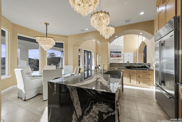 kitchen with sink, a kitchen island with sink, a notable chandelier, decorative light fixtures, and built in fridge