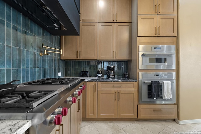 kitchen featuring light tile patterned flooring, wall chimney range hood, stainless steel double oven, dark stone counters, and backsplash