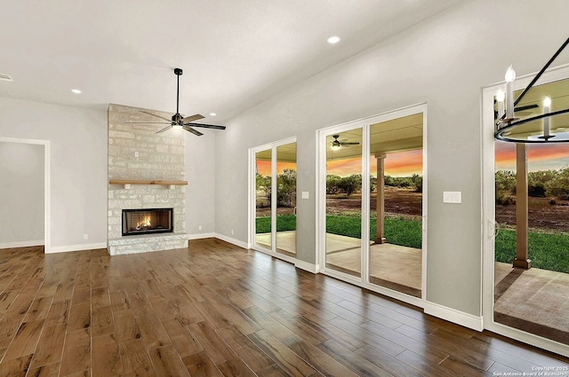 unfurnished living room featuring dark wood-type flooring, ceiling fan, and a stone fireplace