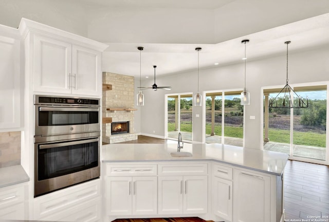 kitchen featuring sink, double oven, a wealth of natural light, a fireplace, and white cabinets