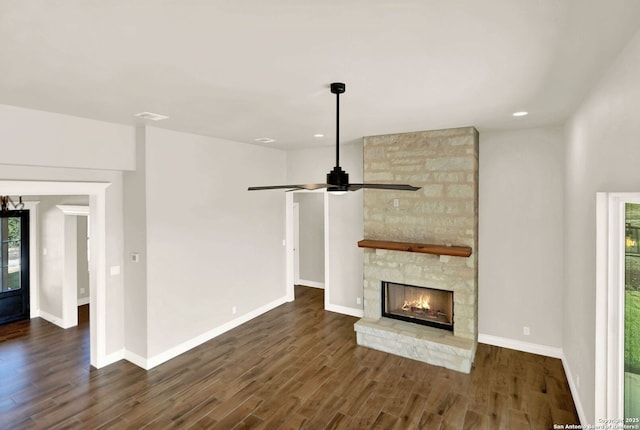 unfurnished living room with ceiling fan, a stone fireplace, dark wood-type flooring, and a healthy amount of sunlight