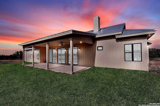 back house at dusk with a patio, a yard, ceiling fan, and solar panels