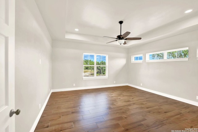 unfurnished room featuring a tray ceiling, dark wood-type flooring, ceiling fan, and plenty of natural light