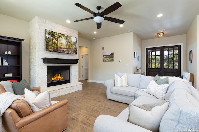 living room featuring ceiling fan, light wood-type flooring, a fireplace, and french doors