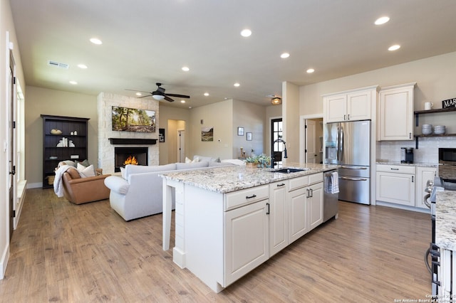 kitchen with white cabinetry, light stone counters, an island with sink, and appliances with stainless steel finishes