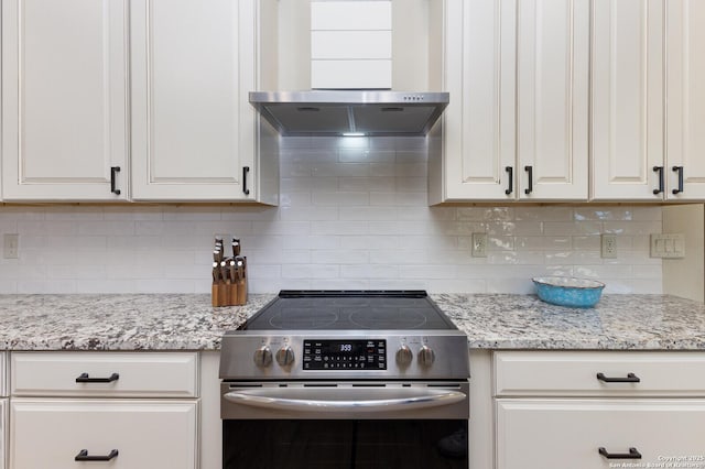 kitchen featuring white cabinetry, light stone counters, stainless steel electric range oven, wall chimney range hood, and backsplash