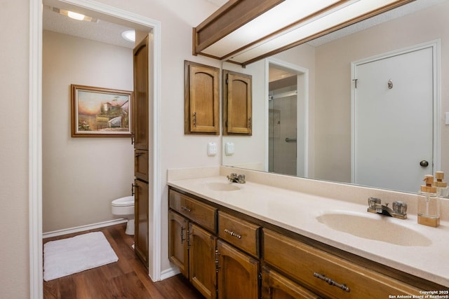 bathroom featuring wood-type flooring, toilet, a shower with shower door, and vanity