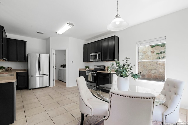 kitchen with pendant lighting, light tile patterned floors, appliances with stainless steel finishes, a kitchen breakfast bar, and washer / dryer