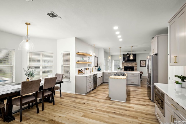 kitchen with gray cabinets, appliances with stainless steel finishes, hanging light fixtures, kitchen peninsula, and light wood-type flooring