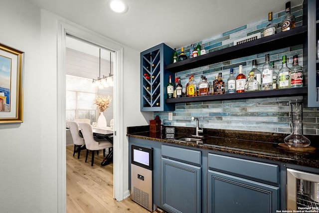 bar with sink, hanging light fixtures, backsplash, beverage cooler, and light wood-type flooring