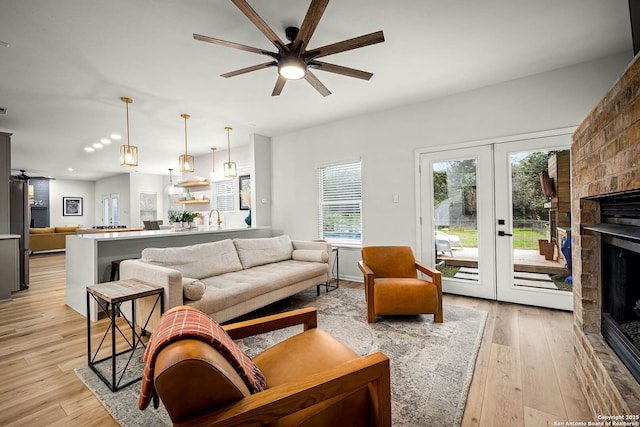 living room with a fireplace, french doors, ceiling fan, and light wood-type flooring