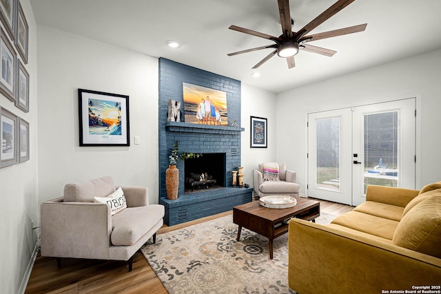 living room with french doors, ceiling fan, wood-type flooring, and a brick fireplace