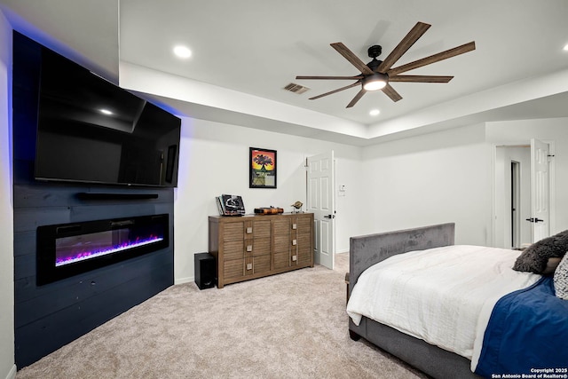 carpeted bedroom with ceiling fan, a tray ceiling, and a large fireplace