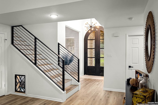 foyer entrance with an inviting chandelier, light hardwood / wood-style flooring, and french doors