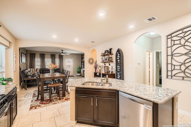 kitchen with sink, light tile patterned floors, a kitchen island with sink, dark brown cabinetry, and stainless steel dishwasher