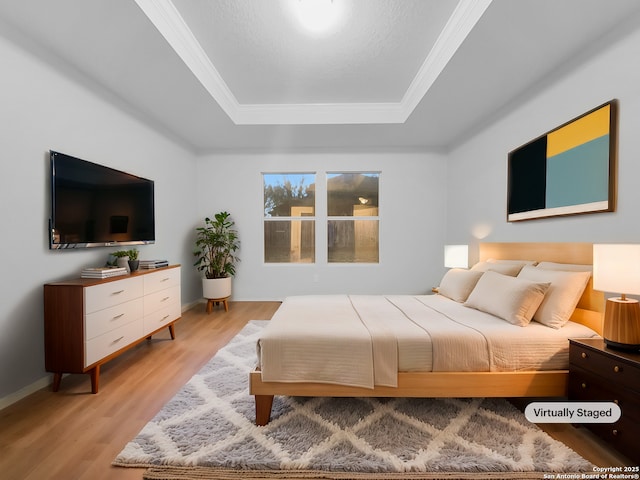 bedroom with ornamental molding, light wood-type flooring, and a tray ceiling