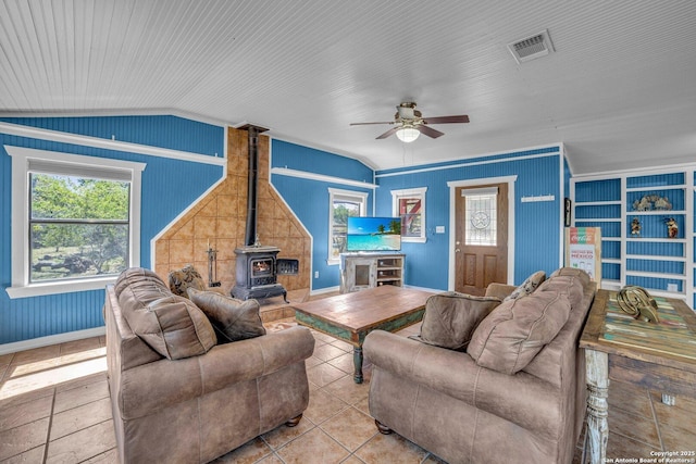 tiled living room featuring lofted ceiling, crown molding, ceiling fan, built in shelves, and a wood stove