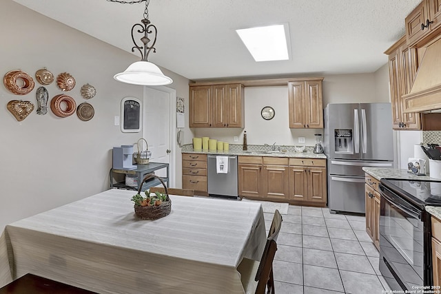 kitchen featuring light tile patterned flooring, appliances with stainless steel finishes, a skylight, custom exhaust hood, and hanging light fixtures