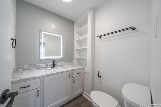 bathroom featuring vanity, wood-type flooring, built in features, and toilet