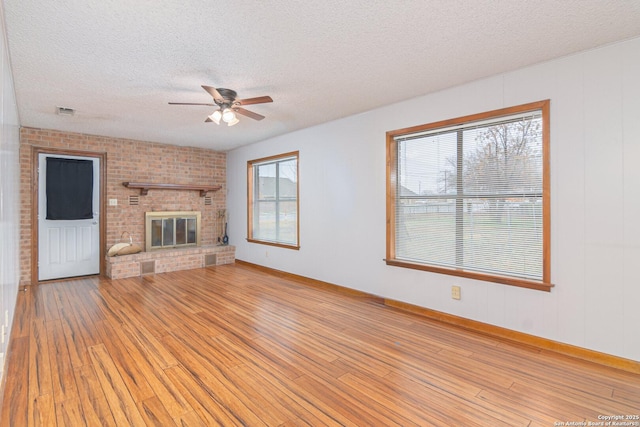 unfurnished living room featuring a brick fireplace, a textured ceiling, a healthy amount of sunlight, and light wood-type flooring