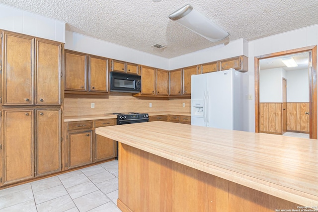 kitchen with wooden walls, light tile patterned floors, a textured ceiling, and black appliances