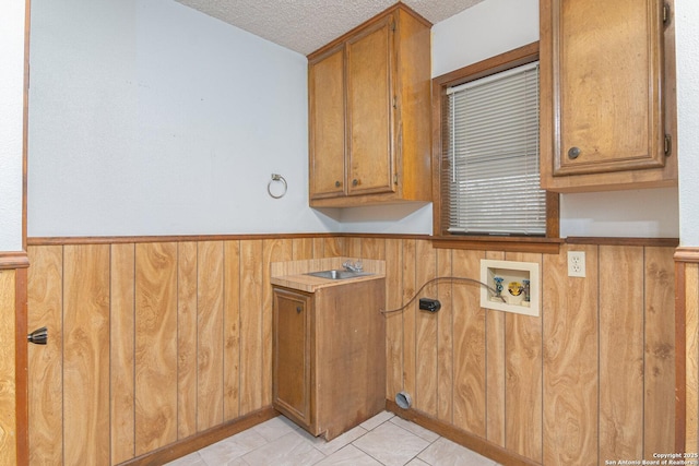 laundry room featuring light tile patterned floors, wooden walls, cabinets, and a textured ceiling