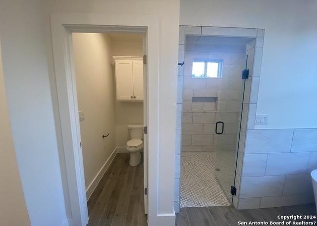 bathroom with hardwood / wood-style flooring, an enclosed shower, and toilet