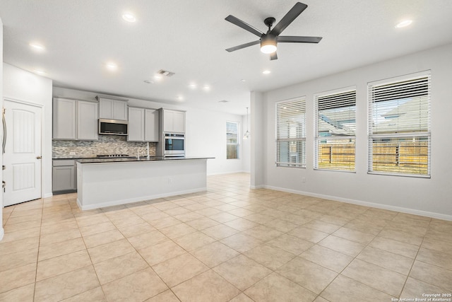 kitchen with gray cabinets, appliances with stainless steel finishes, tasteful backsplash, an island with sink, and light tile patterned flooring