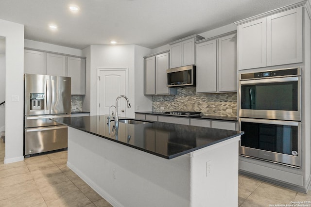 kitchen with appliances with stainless steel finishes, sink, gray cabinetry, and a kitchen island with sink