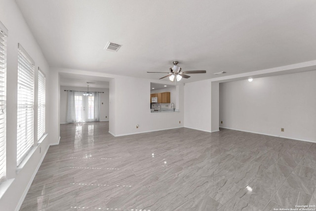 unfurnished living room featuring ceiling fan with notable chandelier