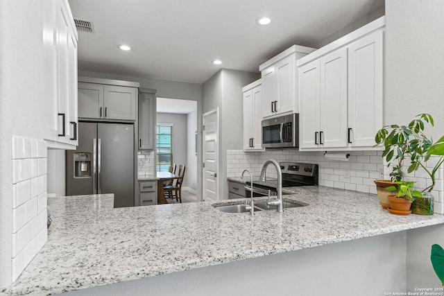 kitchen featuring sink, stainless steel appliances, light stone counters, white cabinets, and kitchen peninsula