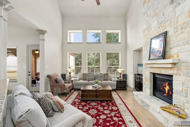 living room featuring a stone fireplace, light tile patterned flooring, a high ceiling, and a healthy amount of sunlight