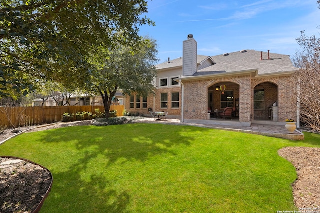 back of house with a lawn, a patio, a chimney, fence, and brick siding