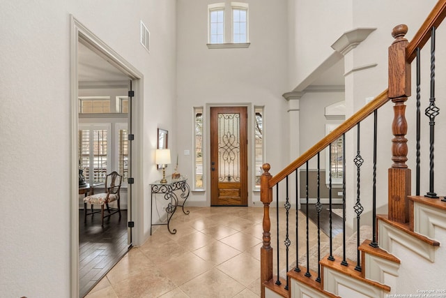 entrance foyer with a towering ceiling, stairs, visible vents, and light tile patterned flooring