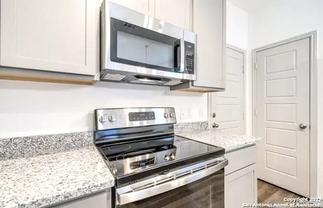 kitchen with white cabinetry, stainless steel appliances, light stone countertops, and light hardwood / wood-style floors