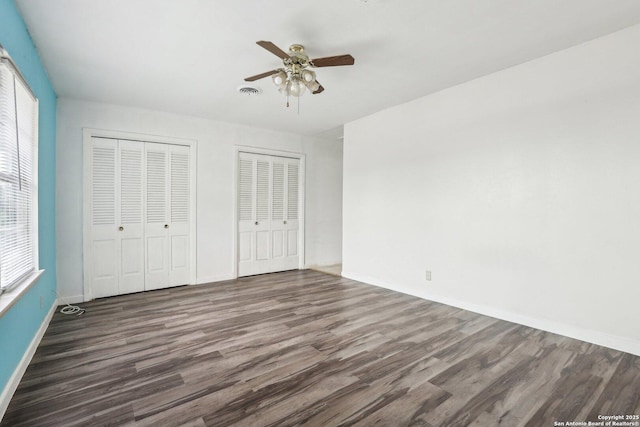 unfurnished bedroom featuring dark hardwood / wood-style flooring, two closets, and ceiling fan