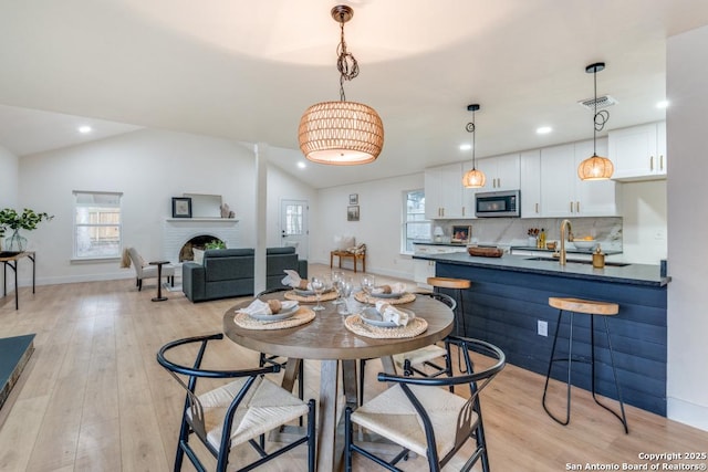 dining room with vaulted ceiling, sink, and light hardwood / wood-style flooring