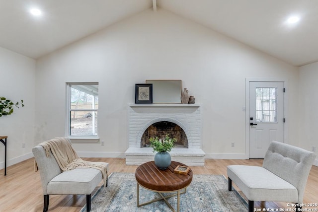 living room with beam ceiling, high vaulted ceiling, a brick fireplace, and light wood-type flooring