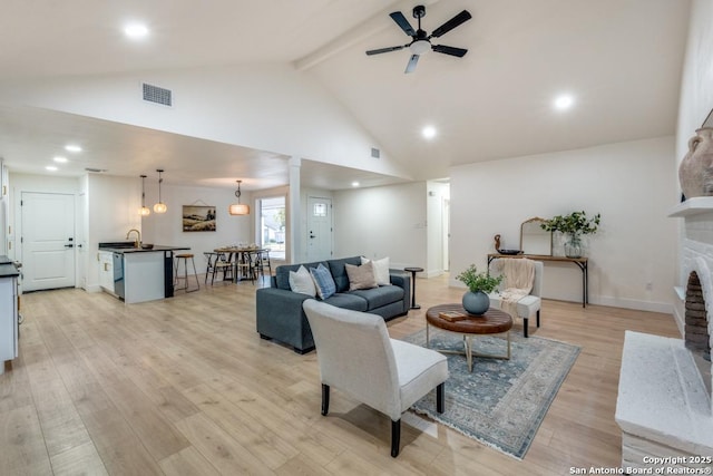 living room with high vaulted ceiling, a brick fireplace, beamed ceiling, ceiling fan, and light hardwood / wood-style floors