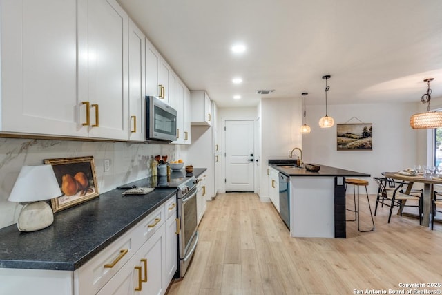 kitchen with stainless steel appliances, a kitchen breakfast bar, decorative backsplash, white cabinets, and decorative light fixtures