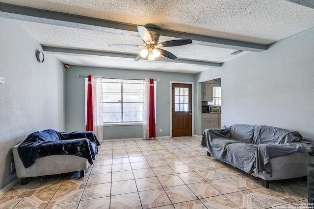 living room featuring beamed ceiling, ceiling fan, light tile patterned flooring, and a textured ceiling